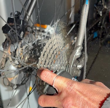 A person spraying degreaser on a mountain bike cassette and chain for bicycle maintenance.