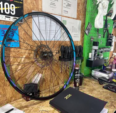 Mountain bike wheel with blue rim tape on a wooden workbench in a bicycle repair shop.