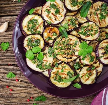 Grilled eggplant slices garnished with fresh herbs on a purple plate