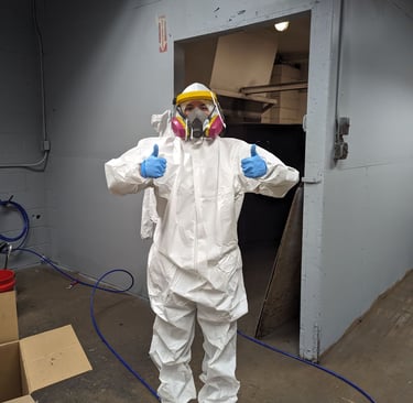 woman wearing protective suit, respirator, gloves, and face shield holding two thumbs up