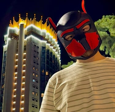 Young man in a pup mask, posing by a tower at night.