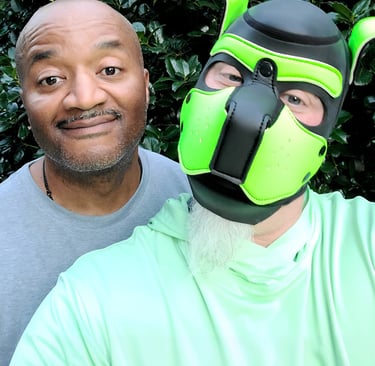 2 Men, 1 wearing a pup mask, posing together.