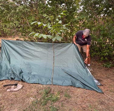 una persona construyendo un refugio de fortuna con un tarp suspendido de una linea de cordino