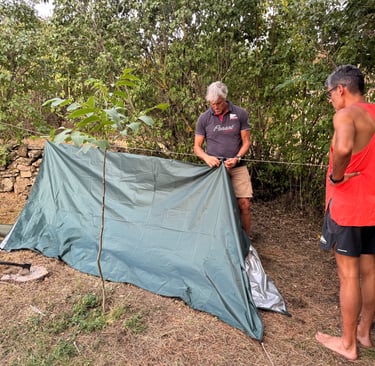 dos personas construyendo un refugio de fortuna con un tarp suspendido de una linea de cordino