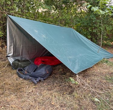 vista exterior de un refugio de fortuna construido con un tarp y línea de cordino