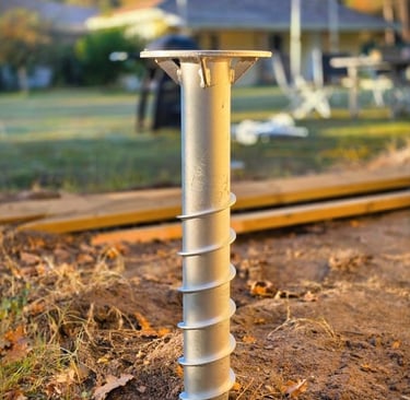 Galvanized steel helical pile foundation screw installed in the ground for deck construction.