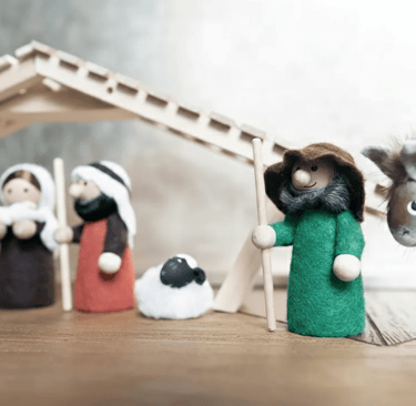 Handcrafted felt nativity scene featuring a wooden stable, shepherds, sheep, and a donkey.