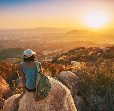 A woman sitting on a rock looking at sunset at peace