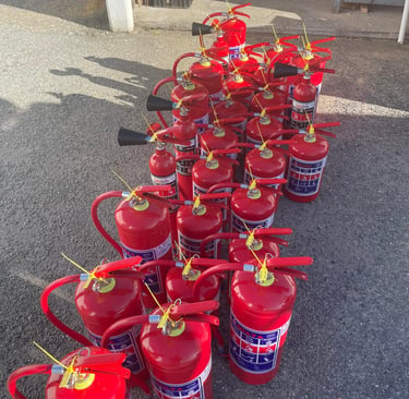 A collection of red portable fire extinguishers arranged on a pavement for inspection or safety maintenance.