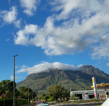 A scenic view of a cloud-capped mountain peak behind a Shell gas station under a blue sky.