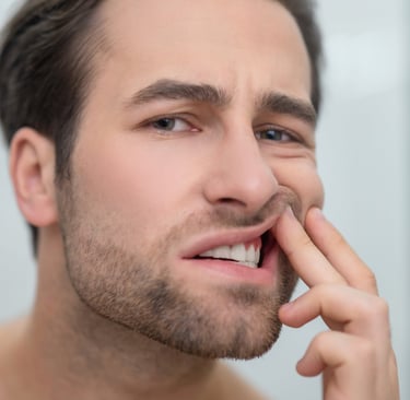 A man examining his red, inflamed gums in a mirror to check for signs of gingivitis or dental pain.
