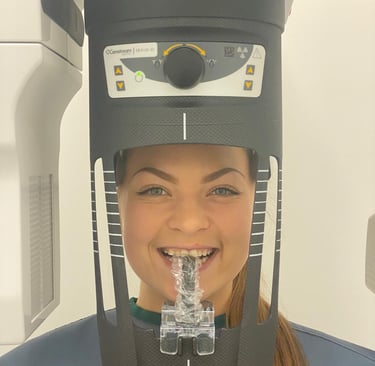A smiling dental patient positioned in a Carestream CS 8100 3D cone beam CT scanner for a diagnostic panoramic x-ray.