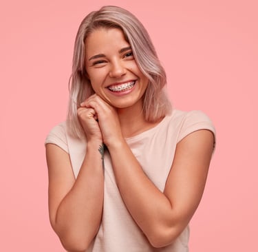 Smiling young woman with silver hair showing dental braces against a pink background.