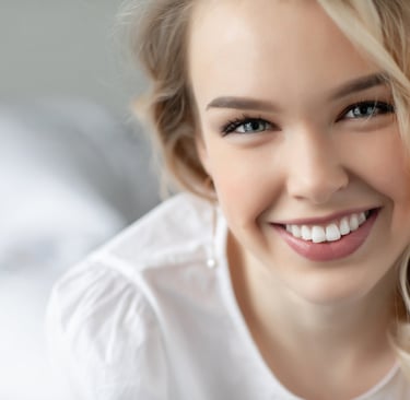 A blonde woman with a bright smile showcasing white teeth and healthy skin in a portrait.