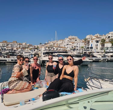 girls raising glasses at the yacht´s bow. Puerto banus marina behind clear blue day