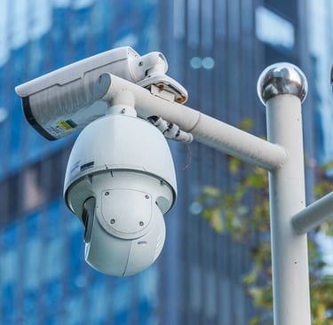 White outdoor PTZ dome security camera and bullet camera mounted on a pole for building surveillance.