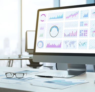view of an office showing charts and graphs on a computer monitor with printouts, a pen and glasses