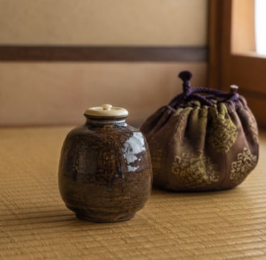 Traditional Japanese ceramic tea caddy and silk drawstring bag on a woven tatami mat.