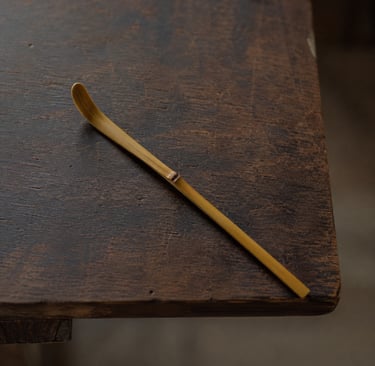 Traditional bamboo matcha tea scoop or chashaku on a rustic dark wooden table.