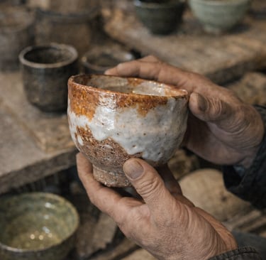 Potter's hands holding a handmade ceramic tea bowl with rustic white glaze in a pottery studio.