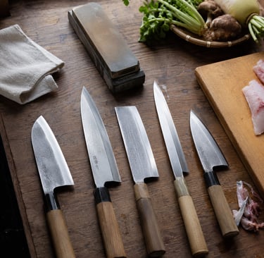Professional Japanese chef knives and whetstone on a rustic wooden kitchen counter with fresh vegetables.