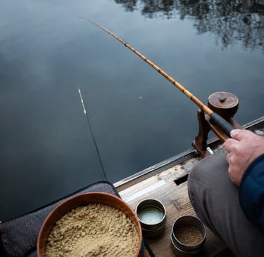 A person using a vintage bamboo fishing rod with bait bowls while fishing on a calm lake.