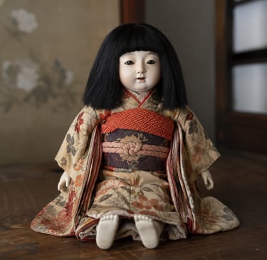 Vintage Japanese Ichimatsu doll wearing a floral silk kimono and obi sash sitting on a wooden surface.
