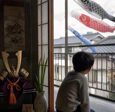 A young boy watches koinobori carp streamers from a Japanese balcony during Children's Day celebrations.