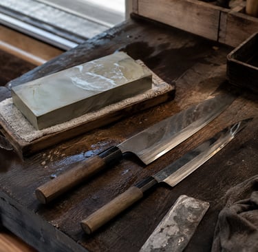 Professional Japanese chef knives and a whetstone sharpening block on a rustic wooden workbench.