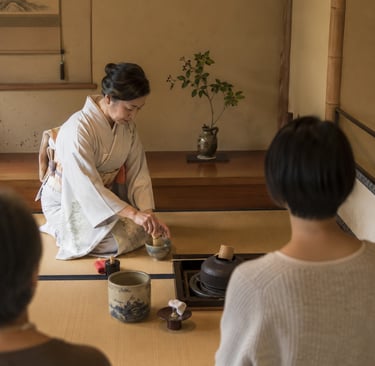 A Japanese woman in a kimono performs a traditional matcha tea ceremony on a tatami mat.