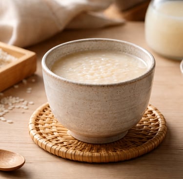 A ceramic bowl of warm Amazake sweet rice drink on a wooden table with raw koji rice.
