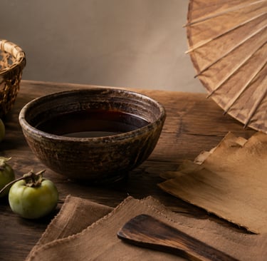 Traditional ceramic tea bowl with green persimmons and a paper umbrella on a rustic wooden table.