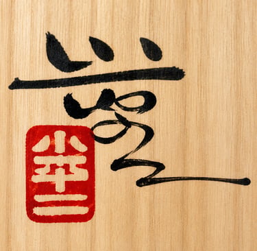 Traditional Japanese calligraphy ink characters and a red hanko seal stamp on a light wood background.