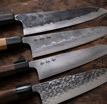 A collection of four handcrafted Japanese chef knives with different steel finishes on a rustic wooden surface.