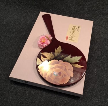 alt="Edler japanischer Handspiegel im Maki-e-Stil mit Blütenmotiv, dekorativ auf rosafarbener Box ar