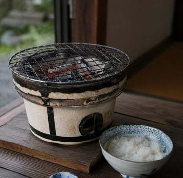 Traditional Japanese shichirin charcoal grill with glowing coals and a bowl of steamed white rice.