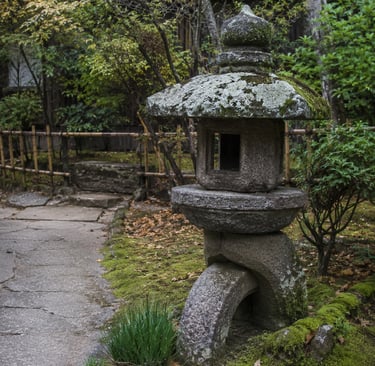 A weathered stone Japanese lantern stands on a mossy path in a serene zen garden setting.