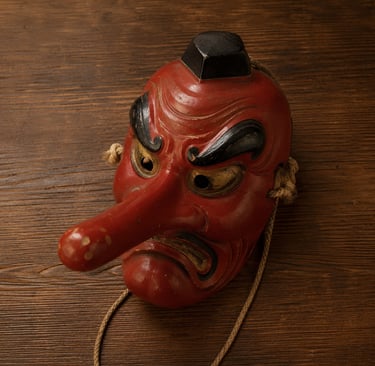 Traditional Japanese red Tengu mask with a long nose and angry expression on a dark wooden background.