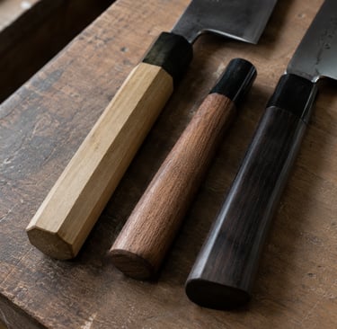 Handcrafted Japanese chef knives with assorted octagonal and round wooden handles on a rustic timber surface.