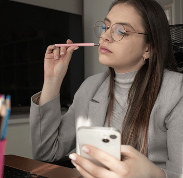 a woman in glasses and a gray sweater is holding a cell phone