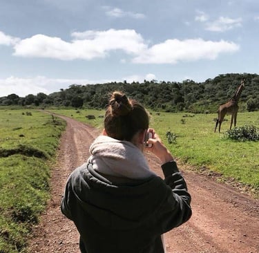 Tourist on a safari trail inside Tarangire National Park holding a camera and photographing a giraffe in its natural wildlife