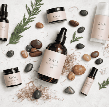 Línea de skincare natural de SAM Cosméticos con frascos, crema facial y tónico sobre fondo con hojas y piedras.