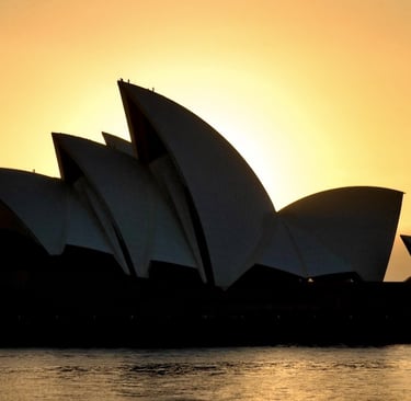 Silhouette of the Sydney Opera House at sunrise against a glowing orange sky over the water.
