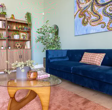 Modern reception room featuring a navy blue velvet sofa, wooden bookshelf, and glass coffee table.