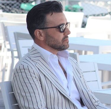 a man in a suit and sunglasses sitting at a table
