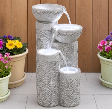 Modern four-tier stone garden water fountain with cascading streams on a patio with potted flowers.