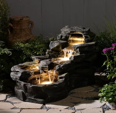 Illuminated rock waterfall fountain with cascading water and LED lights in a garden patio setting.
