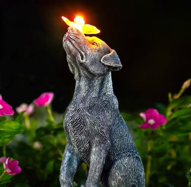 Solar powered dog garden statue with a glowing butterfly on its nose among pink flowers.
