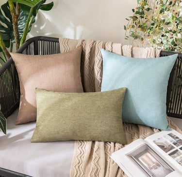 Decorative throw pillows in sage green, tan, and light blue on a stylish outdoor patio chair with a cozy blanket.
