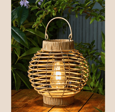 Decorative solar rattan lantern with a glowing Edison bulb on a wooden outdoor table.